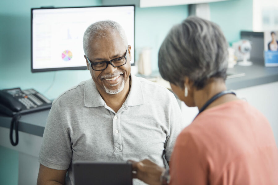 Happy Senior Male Patient Talking To Female Doctor In Clinic