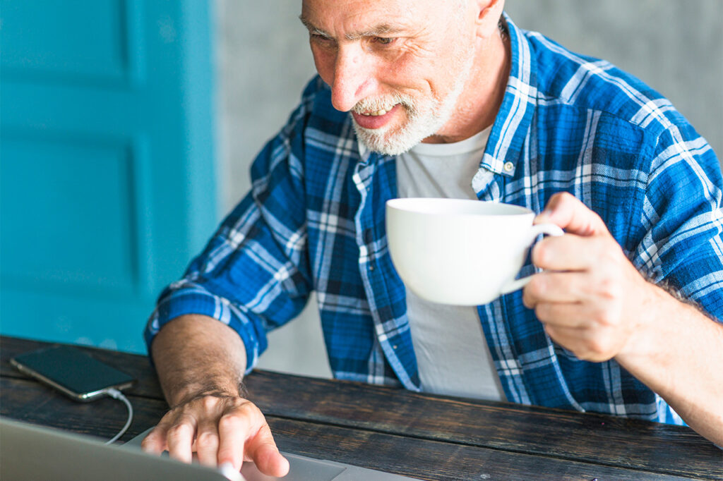 Man Holding Coffee Cup Using Laptop Desk