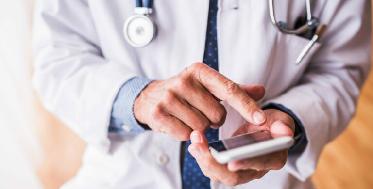 Senior Doctor With Smartphone Working At The Office.