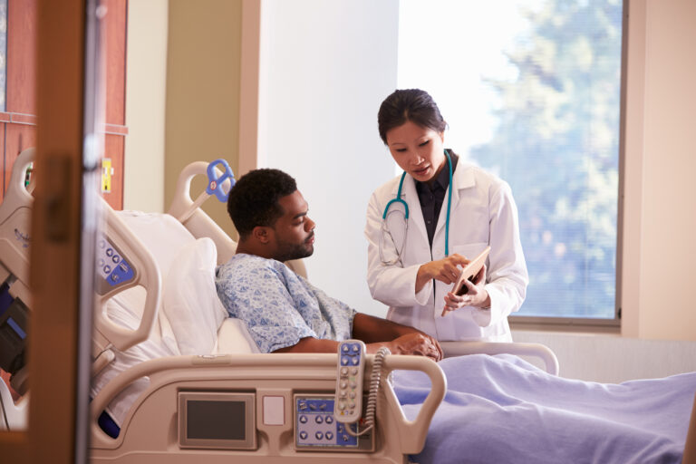 Hospital Doctor With Digital Tablet Talks To Male Patient